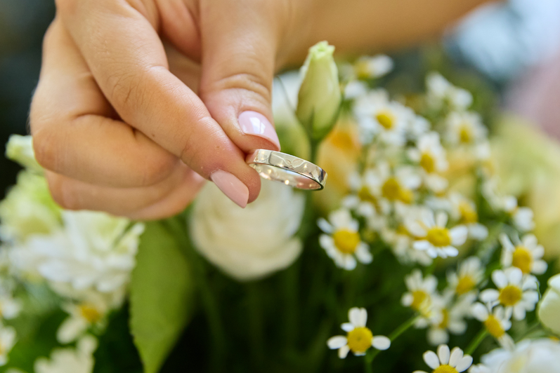 Closeup of someone holding an SFM class ring, flowers are in the background.