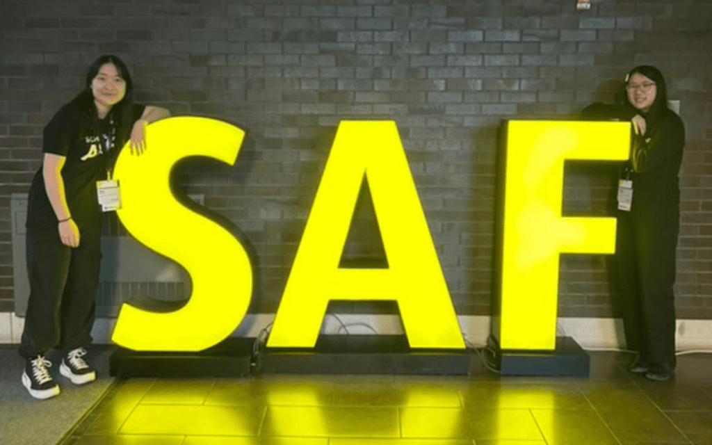Selena and a friend stand on either side of large S-A-F marquee letters