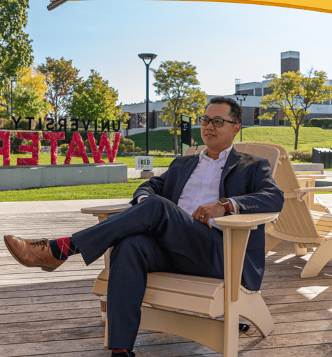 Image of Jonathan Yu sitting in front of the University of Waterloo sign