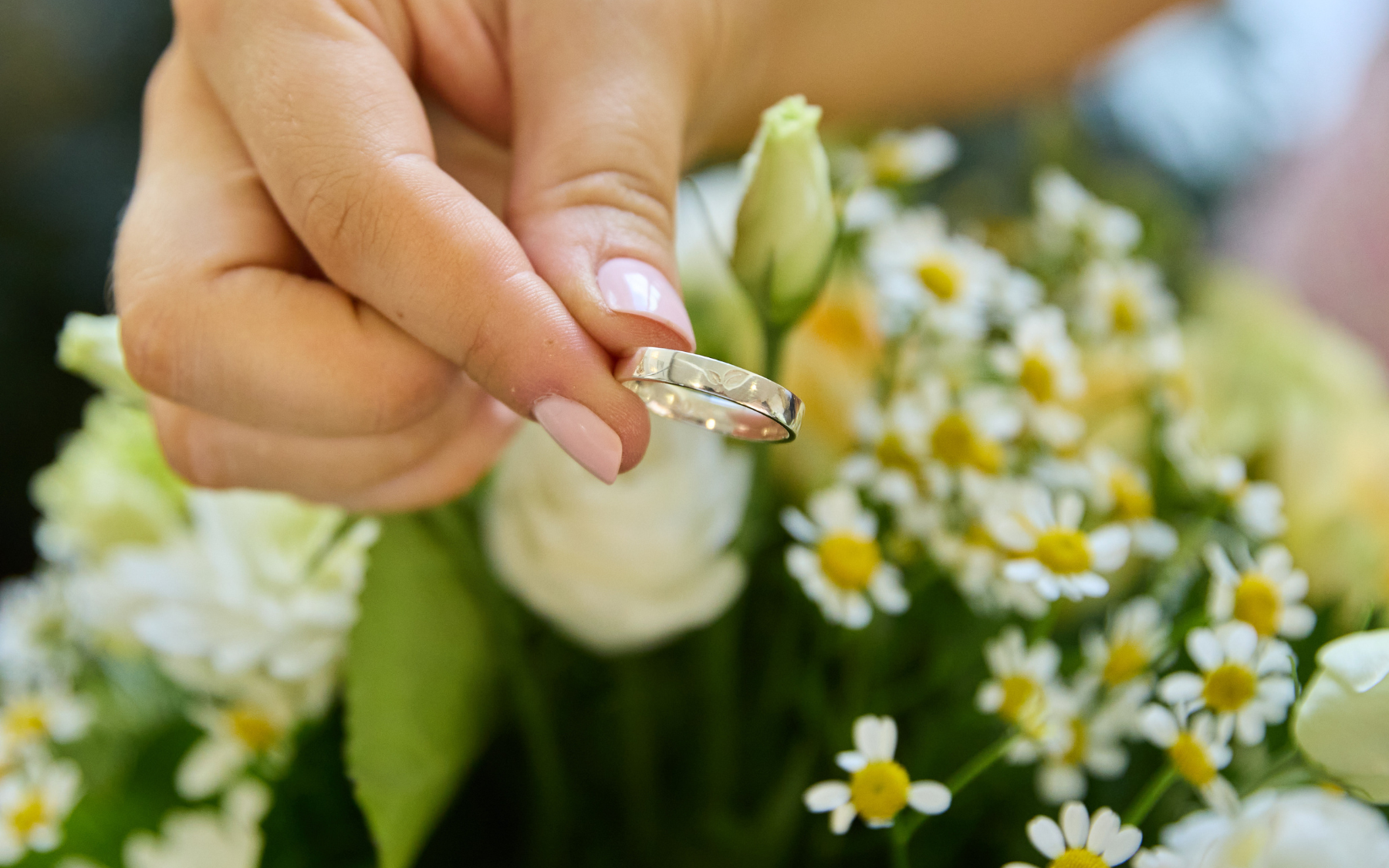 Closeup of someone holding an SFM class ring, flowers are in the background.
