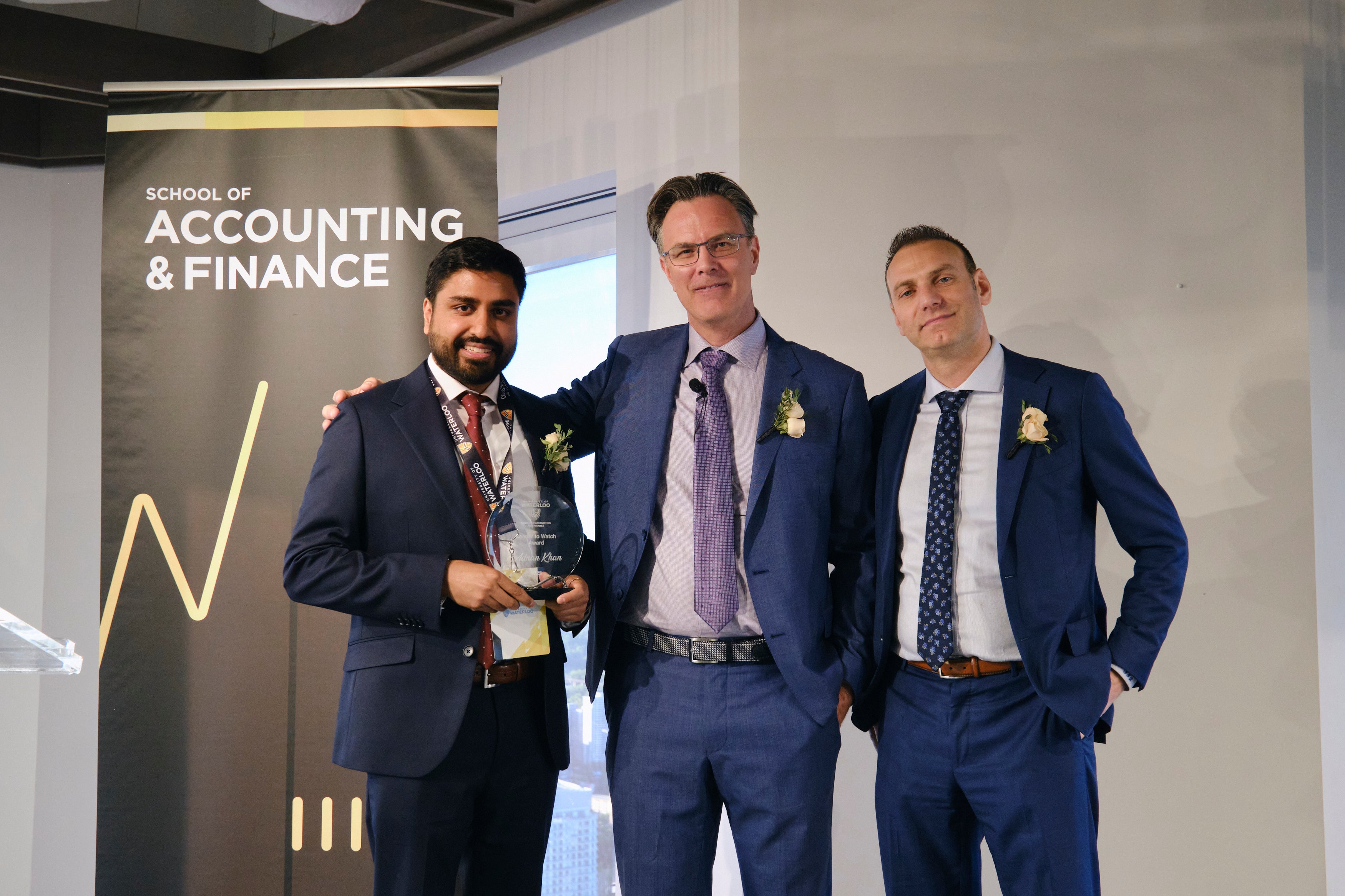 Adnan Khan holds his Leader to Watch Award on stage with SAF Director Blake Phillips and award presenter, Professor Steve Balaban