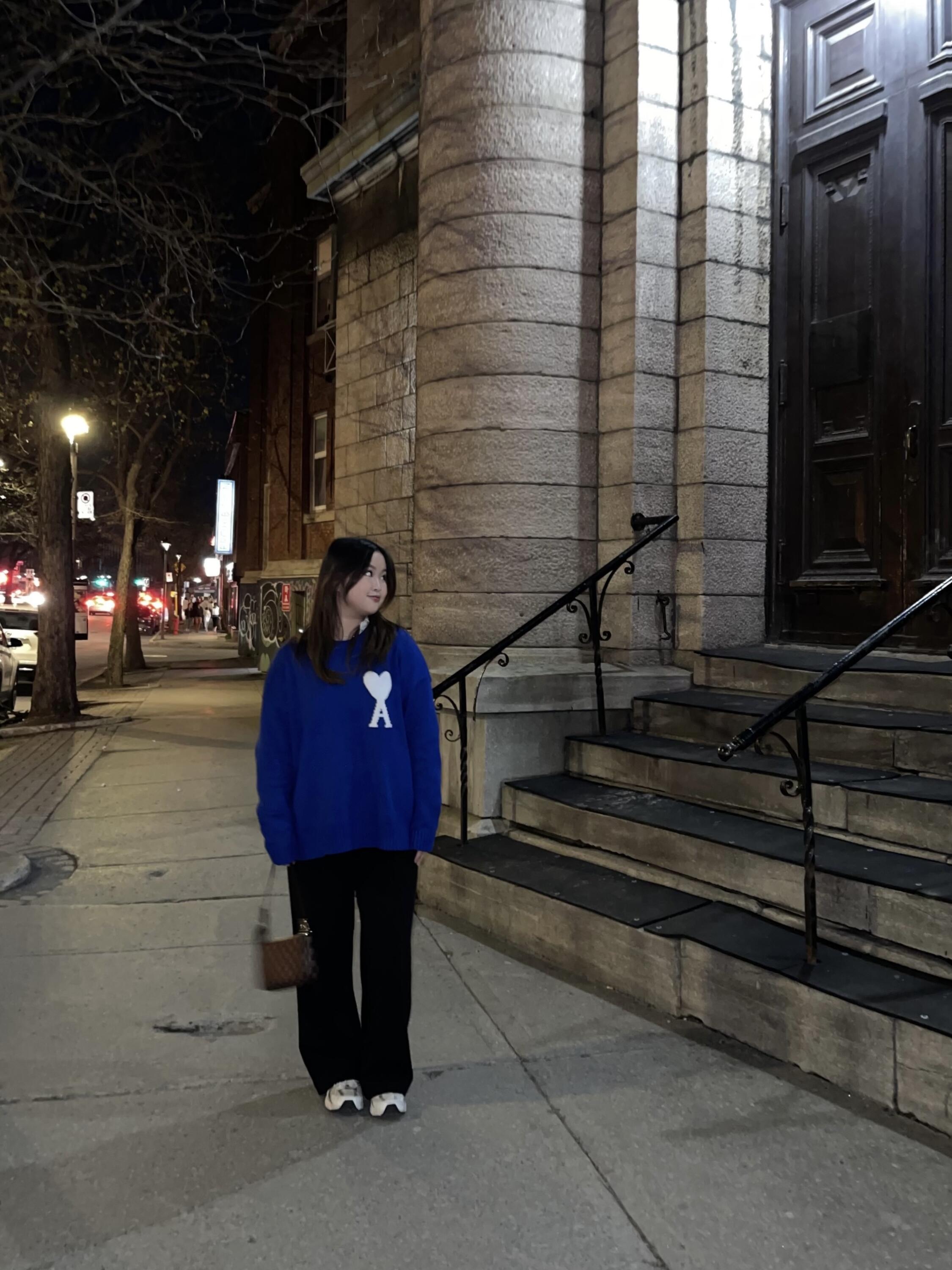 Full body shot of Alyanna standing on the sidewalk by the front of a building