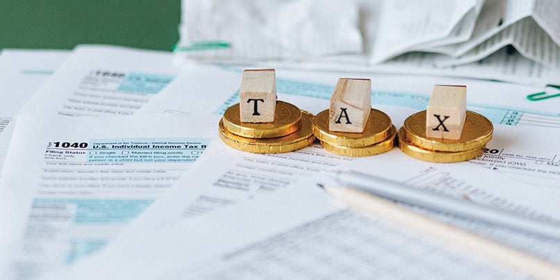 Stacked coins on papers with letters reading "Tax"