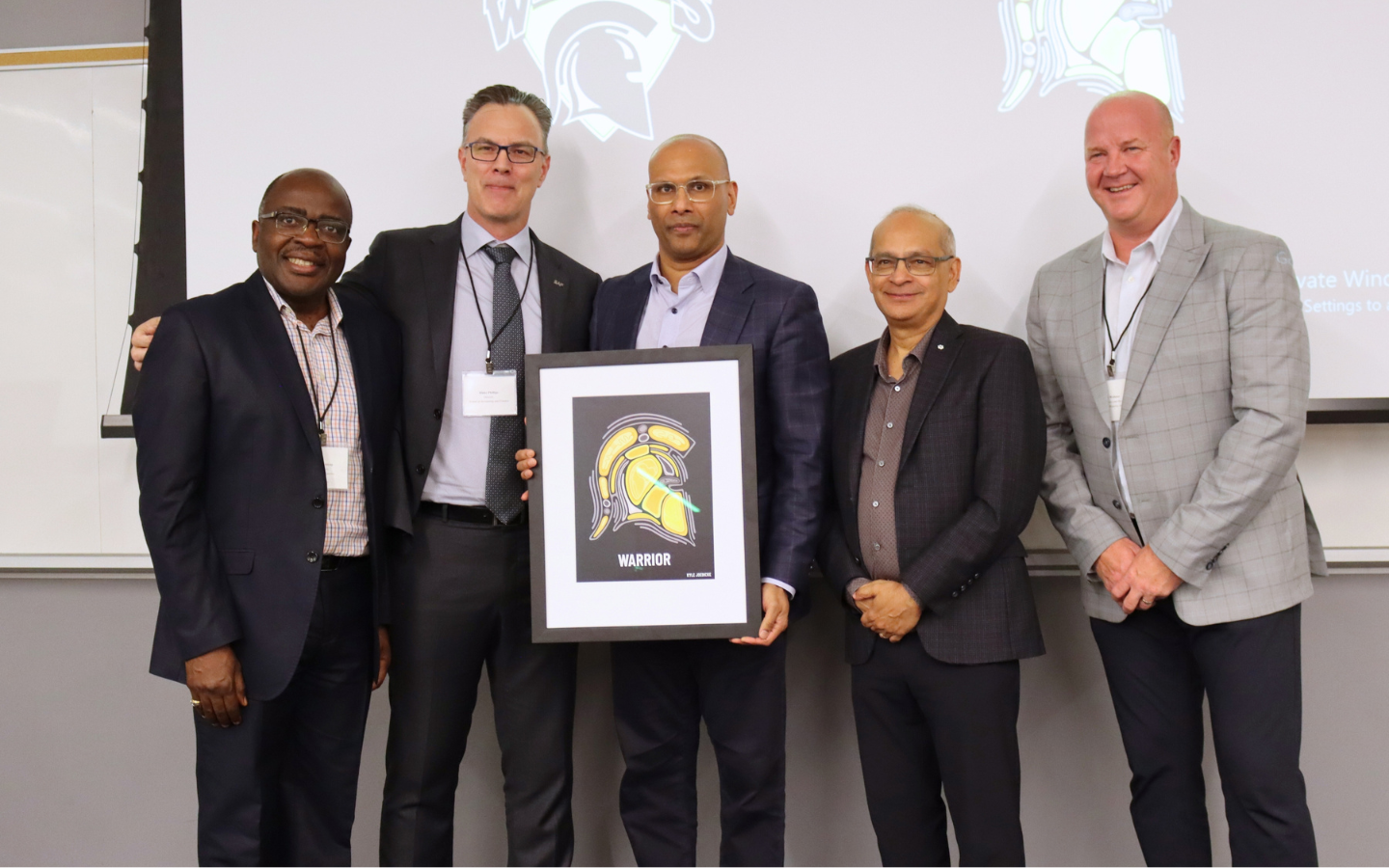 Alexie Tcheuyap, Blake Philips, Benjie Thomas, Vivek Goel and Roly Webster with framed Indigenous Waterloo Warriors logo