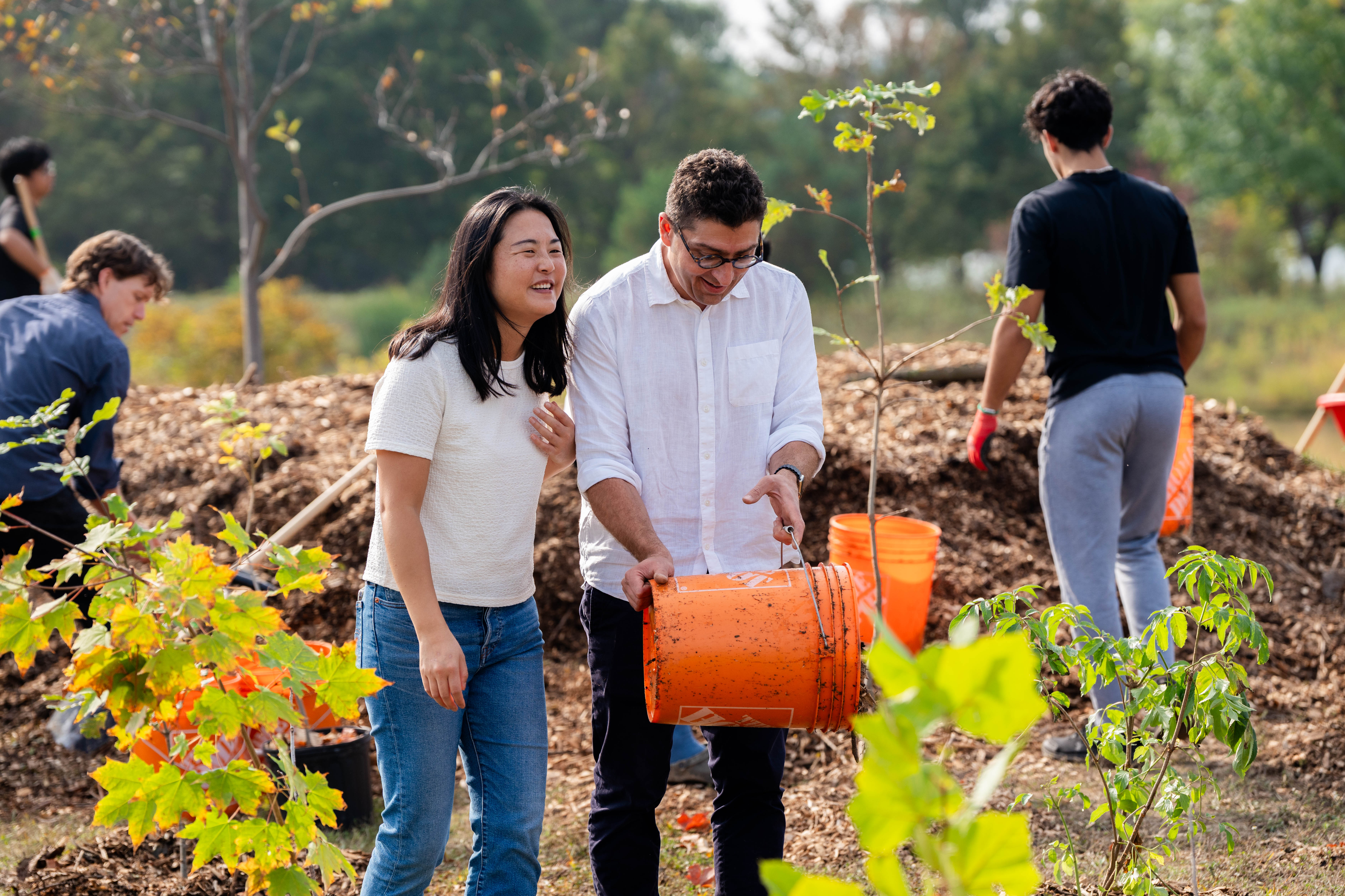 Two SFM faculty members empty a bucket of dirt at the SFM tree planting event