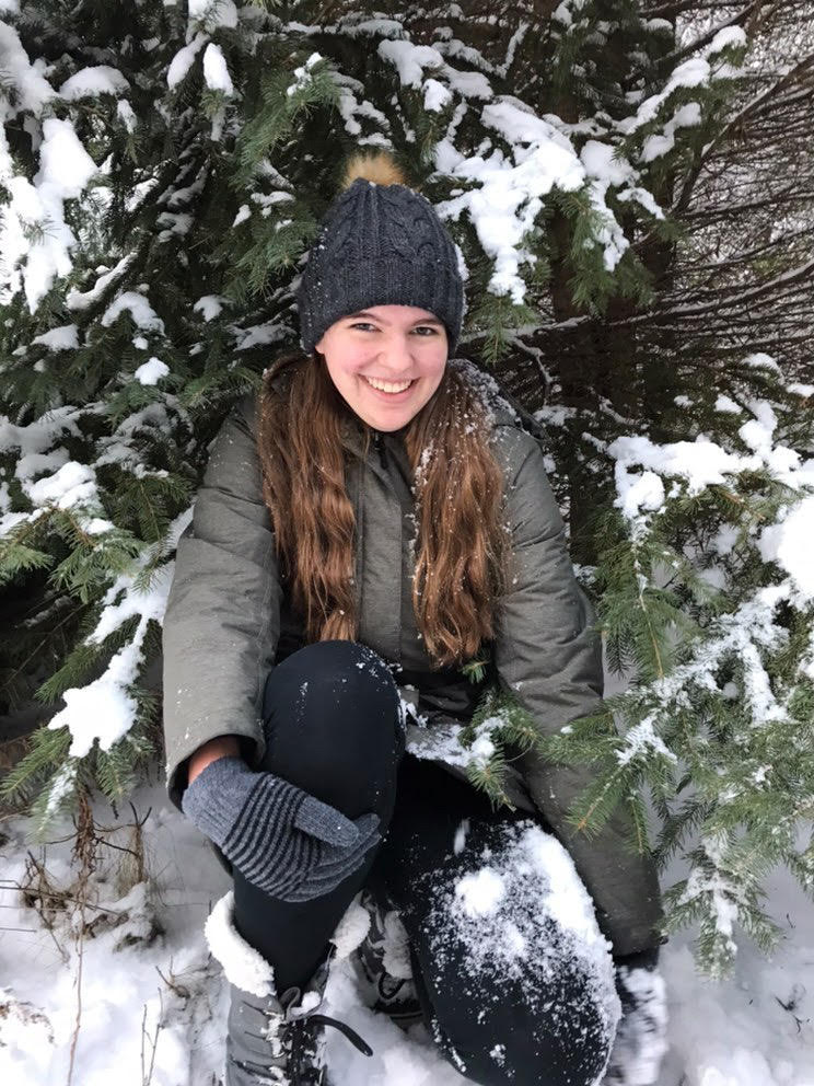 Photo of Claire B. kneeling next to a tree in the winter