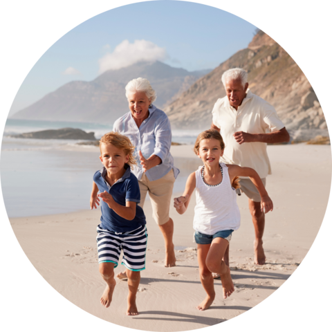 A family of two grandparents and two young kids running on a beach with the ocean and mountains in the background