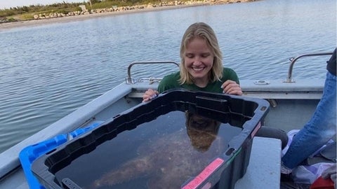 Maya Jacewicz on a boat, looking at a fish in a plastic bin