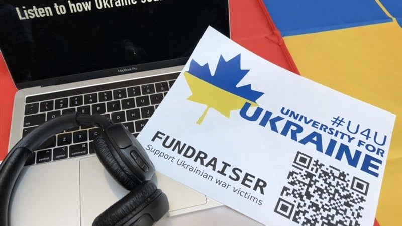 A laptop, headphones, and piece of paper with a QR link to a fundraiser for Ukraine; laptop shows the words “Listen to how Ukraine sounds now”.