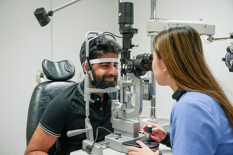 An optemetrist perfoms an eye exam on a man.