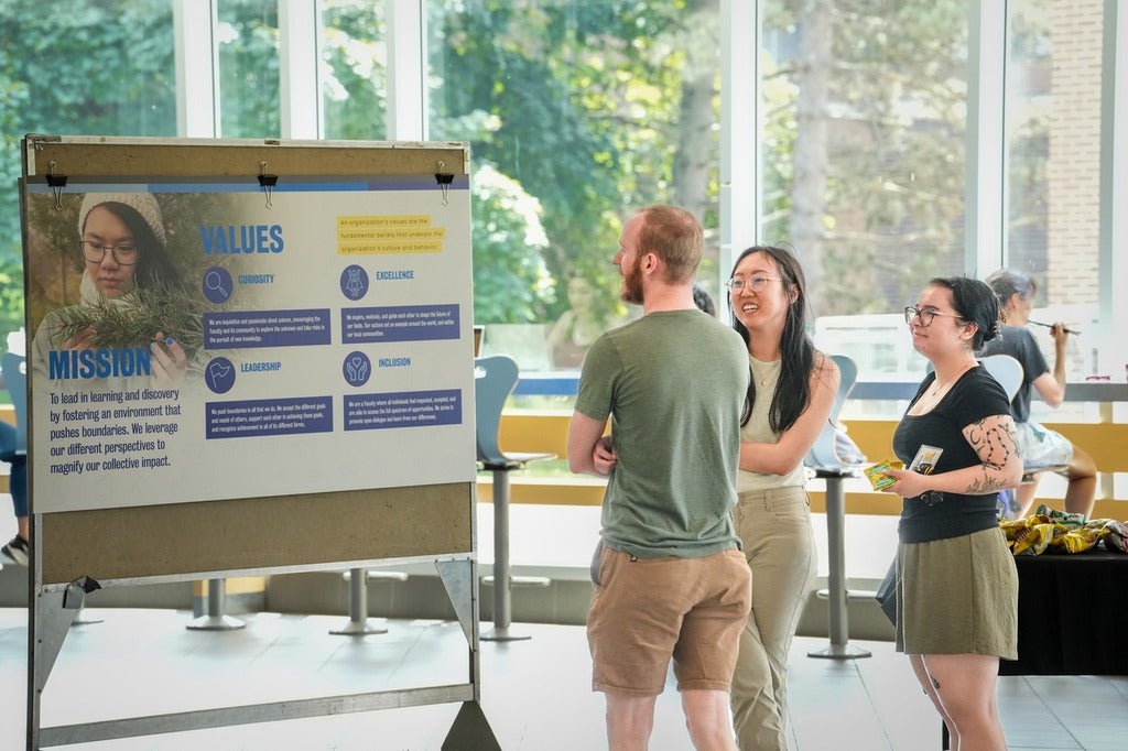 Three students talk while looking at a poster that says "values" and "mission". 
