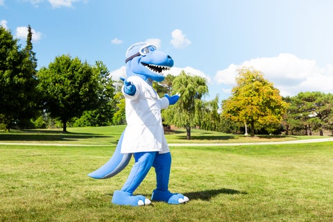 The Science mascot, Cobalt, in a field with their arms open.