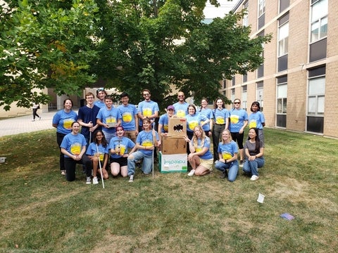 A group of students posing under a tree wearing blue t-shirts.