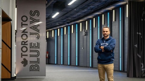 Jeremy Reesor stands with arms crossed outside Blue Jays clubhouse with signage and lighting behind him