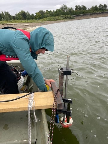 Joey Ruck wearing a raincoat on a boat. He is using a tool to test the water.