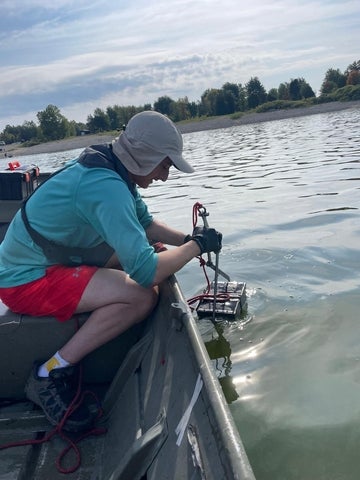 Joey Ruck leaning over on a boat, placing the echosounder in the water.