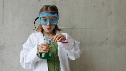 A young child dresses as scientist holding a beaker.