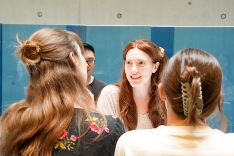 Students chatting against a blue wall. 