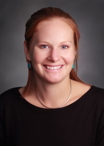 Clare Robinson is wearing a black shirt and smiling to the camera against a black backdrop.