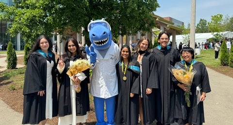 Cobalt surrounded by a group of 6 new graduates wearing their convocation gowns and hoods