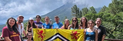 A group of people in Costa Rica with a volcano in the background, holding the University of Waterloo flag