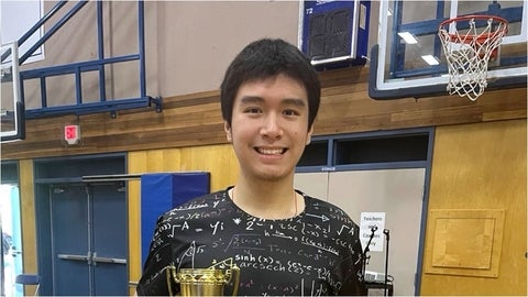 Dio Hsieh standing in a high school gym holding two trophies