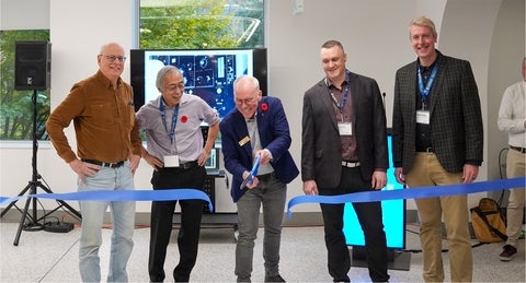 John Corrigan cutting a blue ribbon with giant scissors, standing beside Scott Taylor, Mike Chong, Graham Murphy and Derek Schipper.