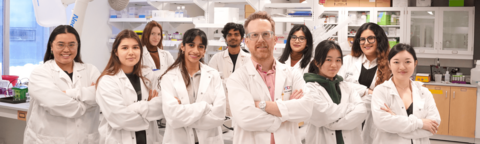 A group of science students posing with their arms crossed in white lab coats in a lab setting at the University of Waterloo.