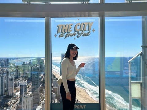 Tiffany Chan in Australia pointing to a view of the beach from a tall building. 