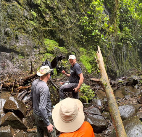 Chris Houser leading alumni on a hike across a stream in the rainforest