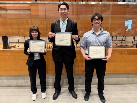 Three students holding their award certificates at the conference. 