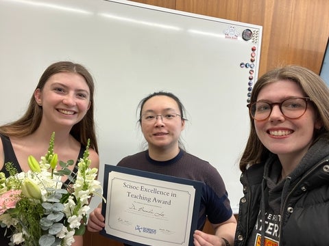 Dr. Brenda Lee receiving award with two female students on either side of her. 