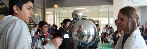 Two students play with an electrostatic generator at an open house event.