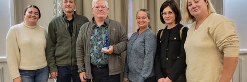 Dr Mark Servos is holding an award in his hands as he stands with past and current students