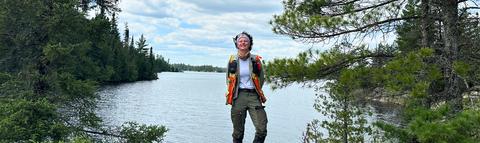 Nathalie standing at the edge of a lake in Northern Ontario surrounded by trees.
