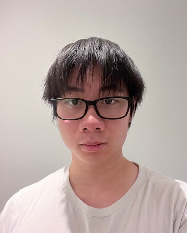 Percy Luk wearing a white t-shirt against a white background. He is wearing black glasses and has short dark brown hair. 