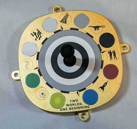 A gold disk with four screw holds on it, showing a black and white bulls eye in the centre surrounded by 8 circular colour panels separated by images of an atom, DNA strand, cyanobacteria, a fern, a dinosaur, humans and a rocket ship