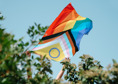 A Pride flag waving in the wind against a blue sky