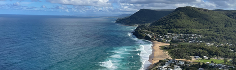 A wide coastal view of Australia showing deep blue ocean on the left and a sandy beach curving along the shoreline.