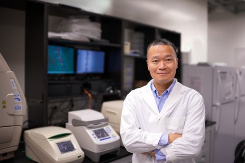 Dr Juewen Liu is wearing a lab and standing with his arms crossed against the backdrop of his lab.