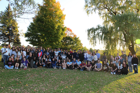A large group photo of the Science Society bondfire outside in a park on a sunny evening.