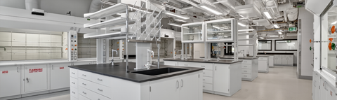 A bright, modern science laboratory with white cabinets, black countertops, and central island workstations.