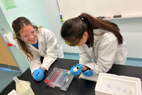 A university student showing a high school student how to do a science experiment.