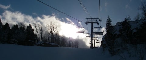 A chair lift above a ski hill covered in snow and lined with pine trees