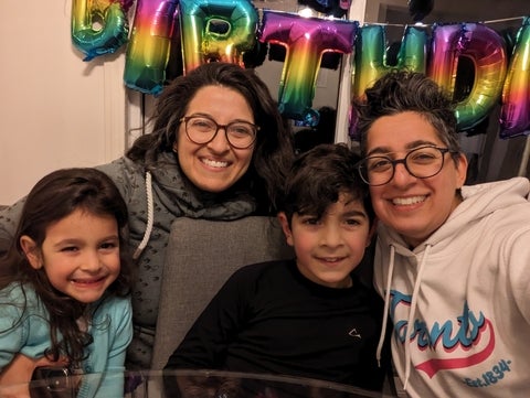 Sophia and their family smiling at the camera in front of birthday balloons. 