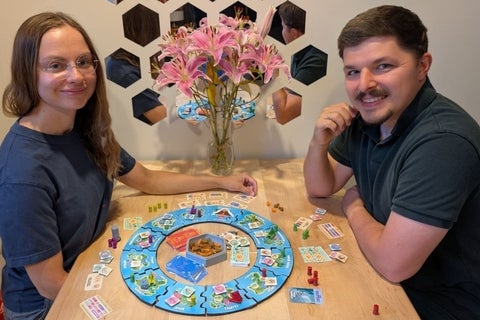 a woman and man sitting at a table playing a circular boardgame
