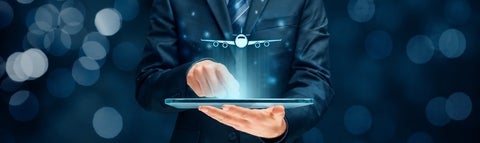 Man in a suit holding a laptop with an airplane projected above. 
