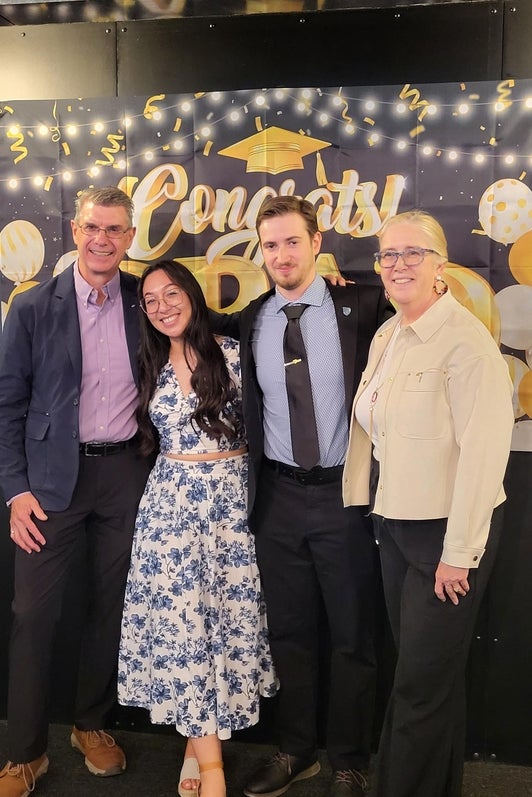 Two undergraduate students posing with professors of Chemistry in front of a graduation sign. 