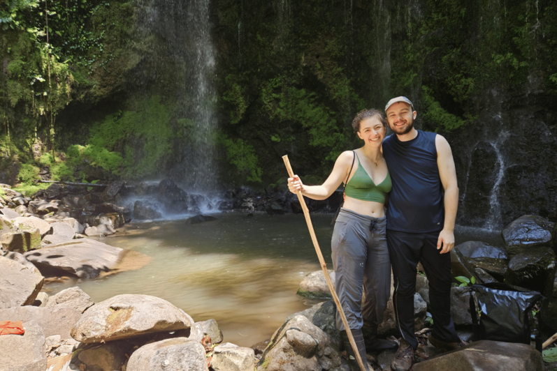 Daniel and Liv standing next to a waterfall and swimming hole.