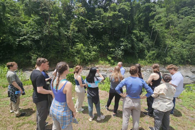 A group of students being taught by Dean Chris Houser outside of a rainforest.
